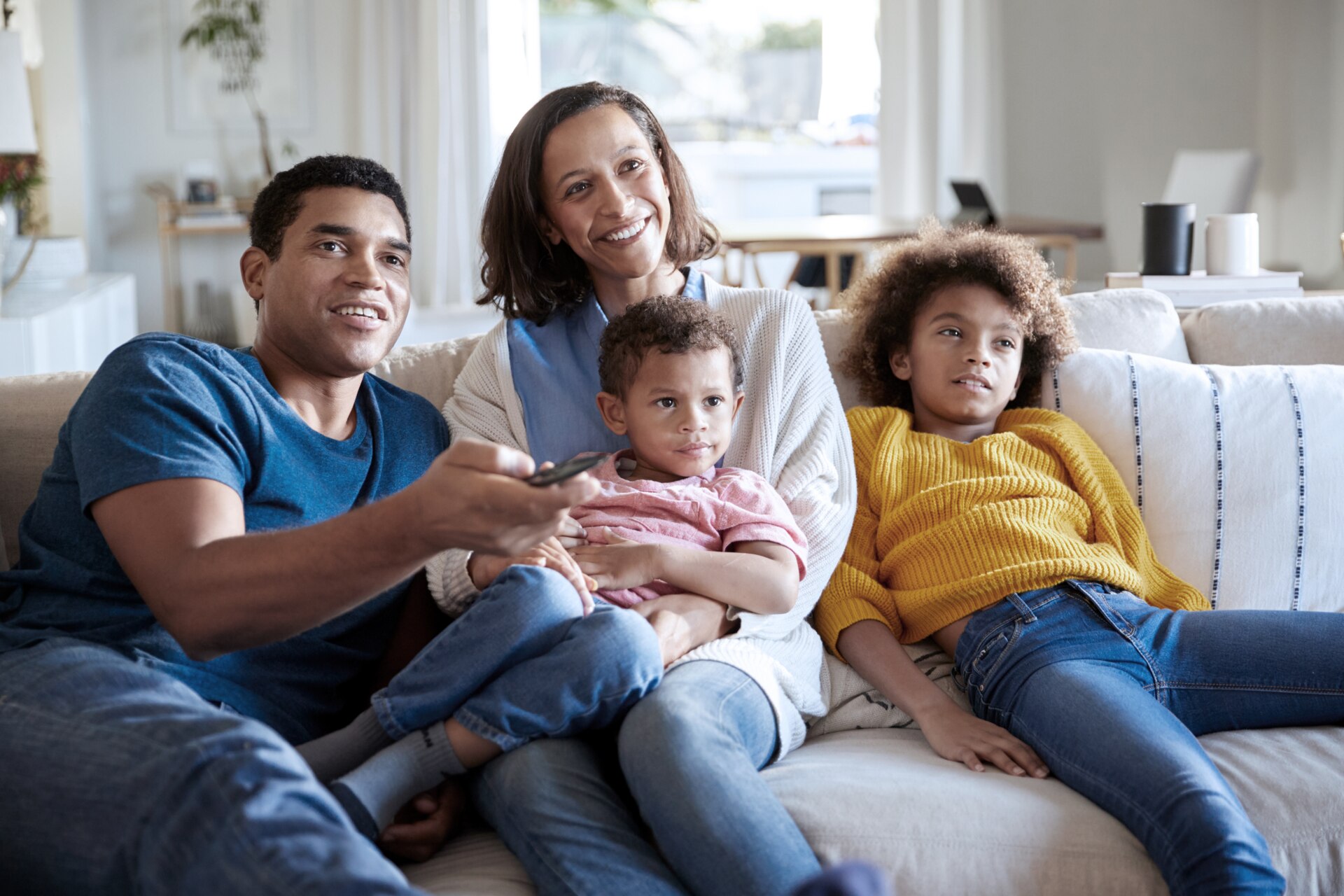 A happy family sits on the couch while the father points a remote control at the TV. A happy family sits on the couch while the father points a remote control at the TV.