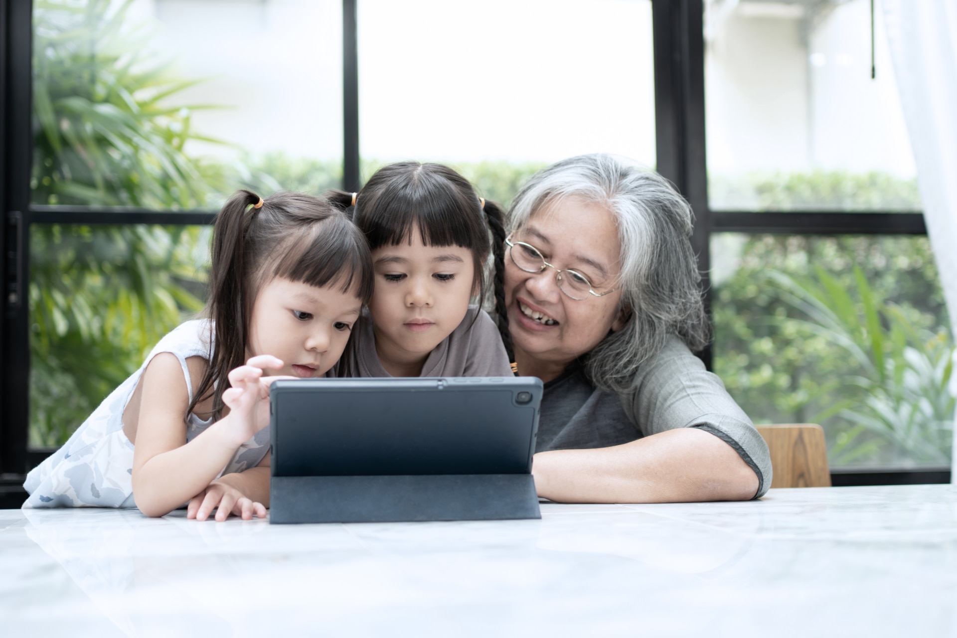 A grandmother watches her two grandchildren use a tablet. A grandmother watches her two grandchildren use a tablet.