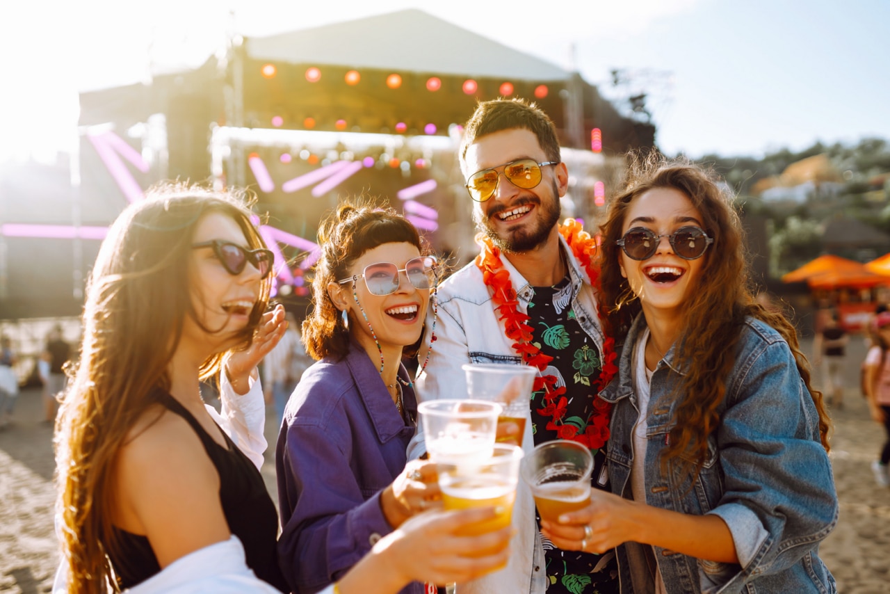 Young happy friends drinking beer and having fun at music festival together. 