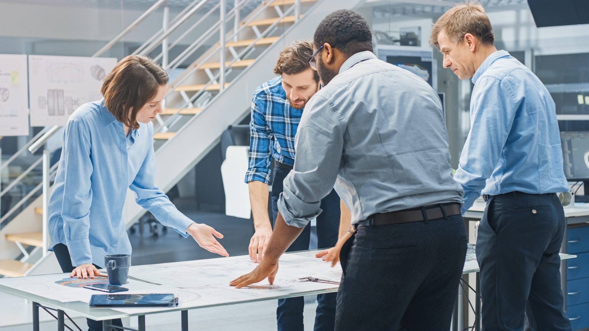 In the Industrial Engineering Facility: Diverse Group of Engineers and Technicians on a Meeting Gather Around Table Unravel Sheets of Engine Design Technical Drafts, Have Discussion, Analyse Drawings.; Shutterstock ID 1515843497; purchase_order: -; job: -; client: -; other: -