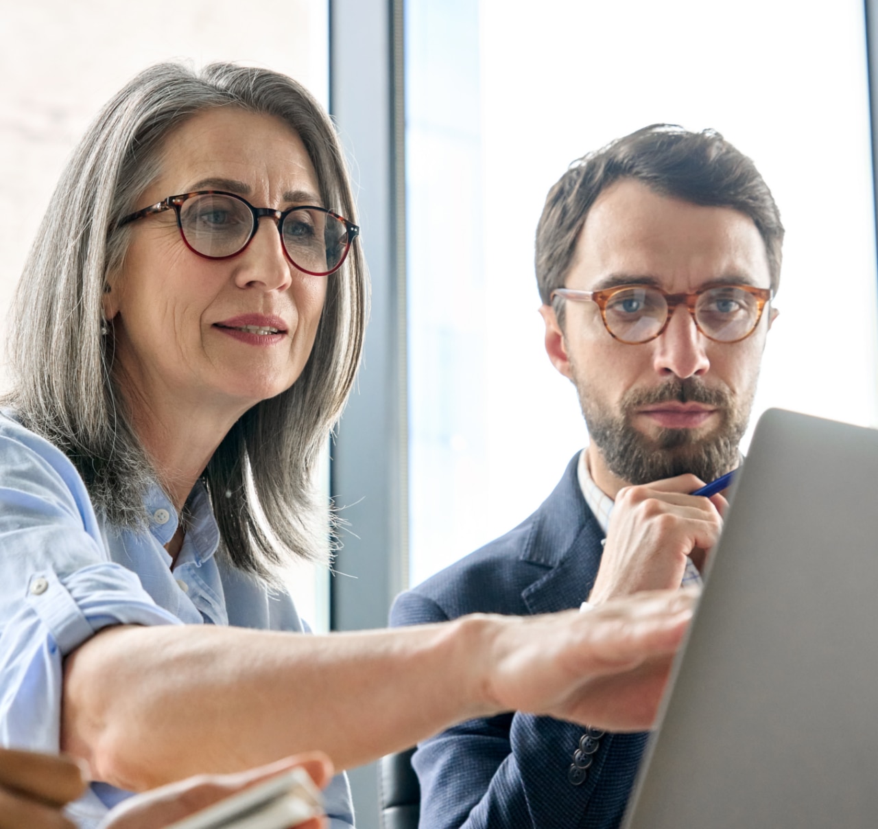 Mature older ceo businesswoman mentor in glasses negotiating growth business plan with diverse executive managers at boardroom meeting table using laptop. Multicultural team work together in office.; Shutterstock ID 2025930416; purchase_order: 1100061200; job: 600704; client: Carolin Calefi Dias; other: Phonak