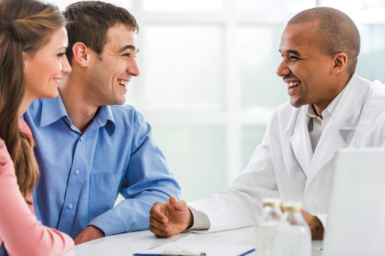 Cheerful African American doctor communicating with young couple in doctor's office.