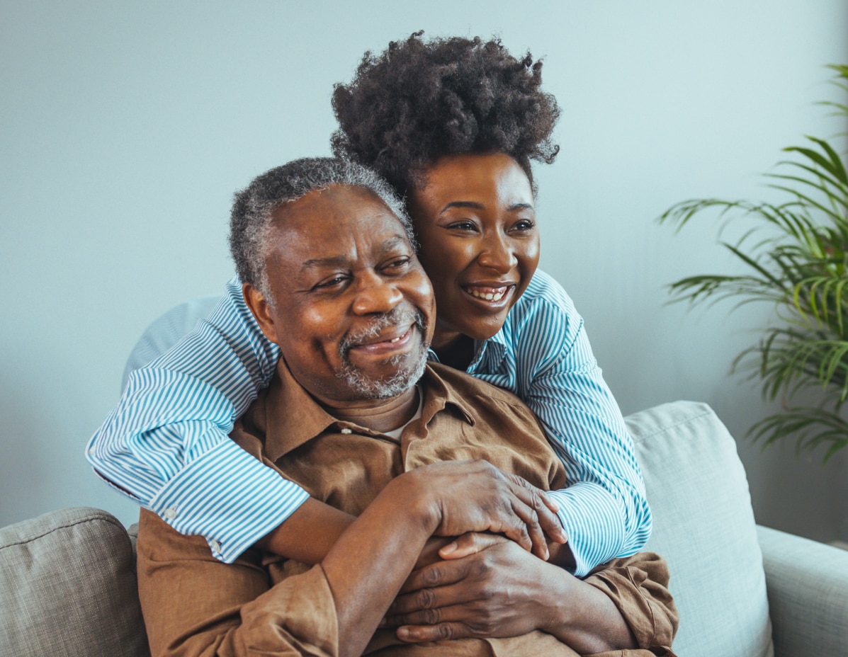 Adult daughter visits senior father in assisted living home. Portrait of a daughter holding her elderly father, sitting on a bed by a window in her father's room