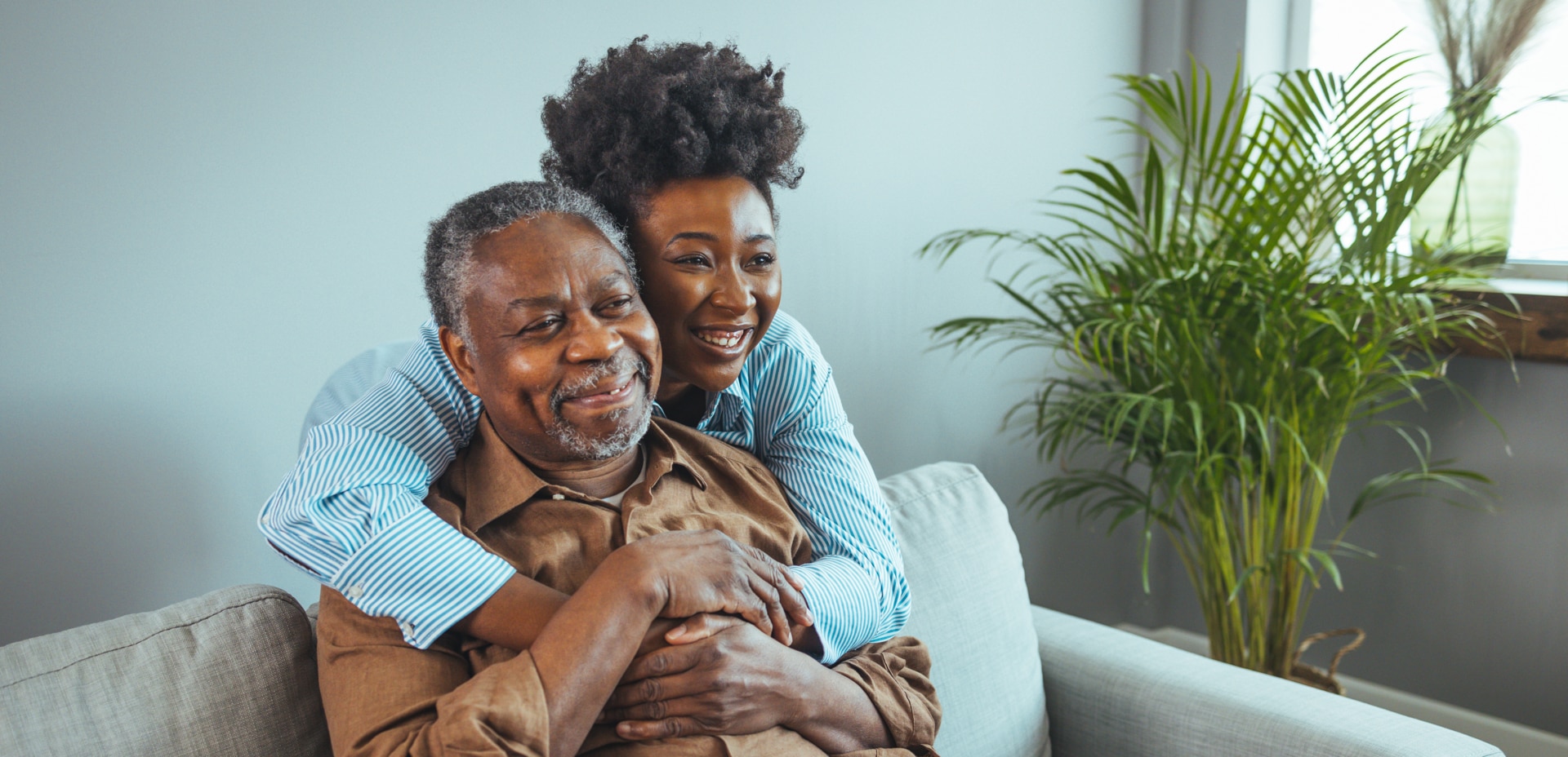 Adult daughter visits senior father in assisted living home. Portrait of a daughter holding her elderly father, sitting on a bed by a window in her father's room