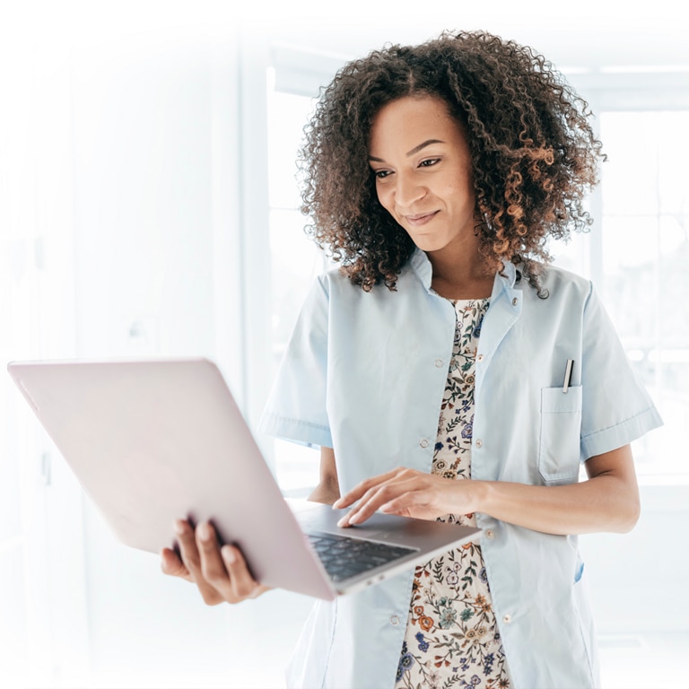 Mulher em pé em um ambiente interno com o seu laptop na mão.