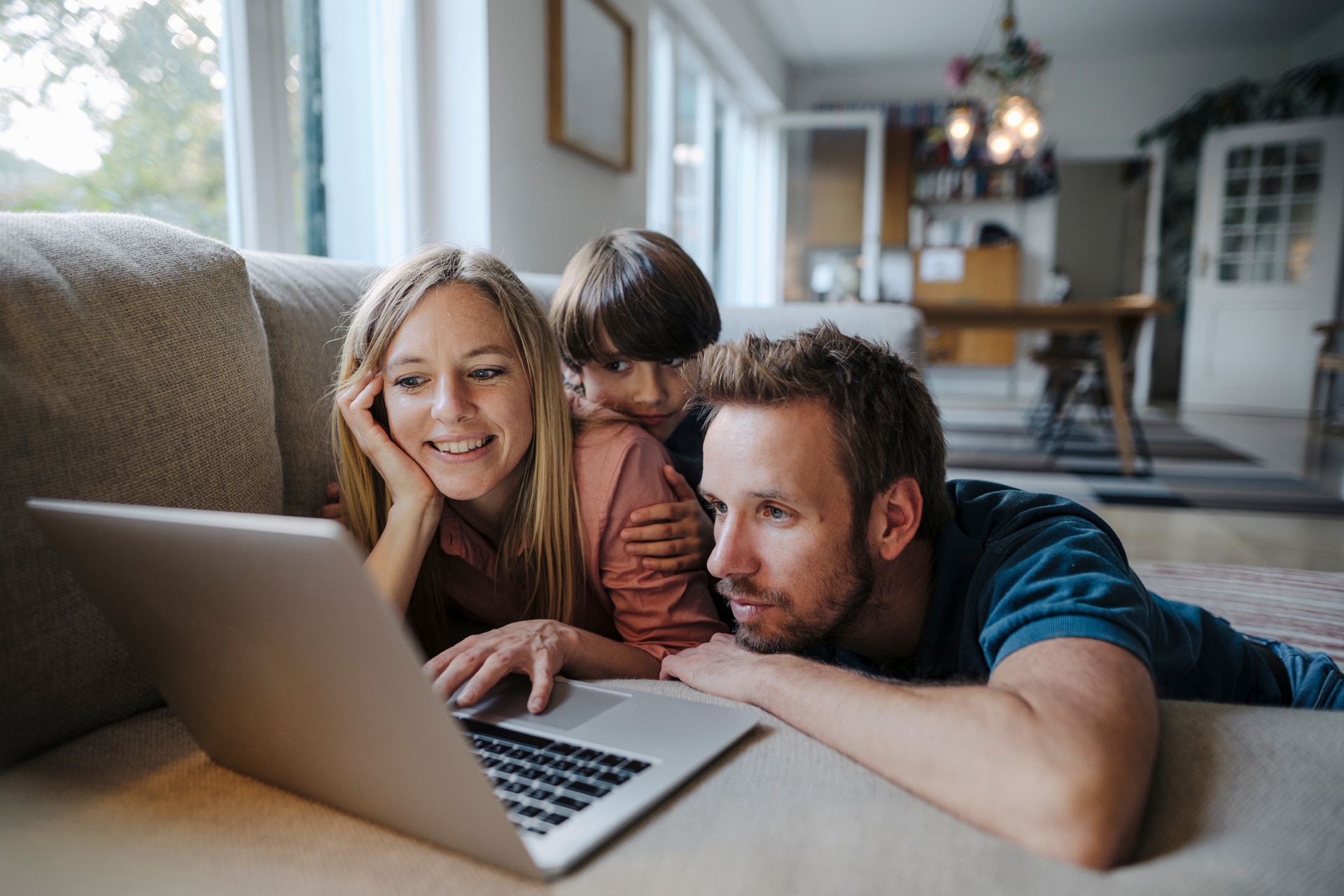 Happy family lying on couch- using laptop