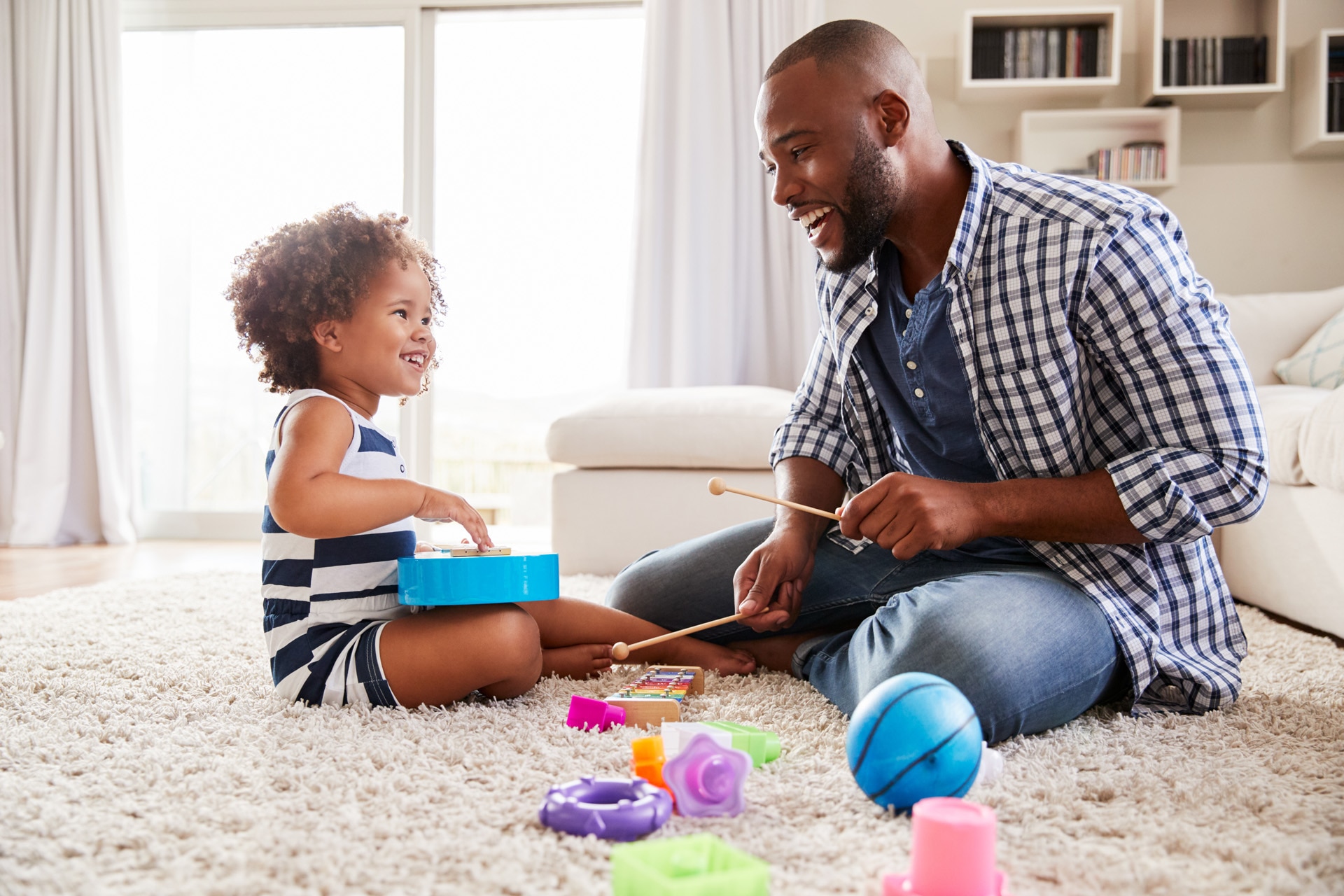 Pai jovem brincando a sua filha pequena com instrumentos musicais simples – cena dentro de casa.