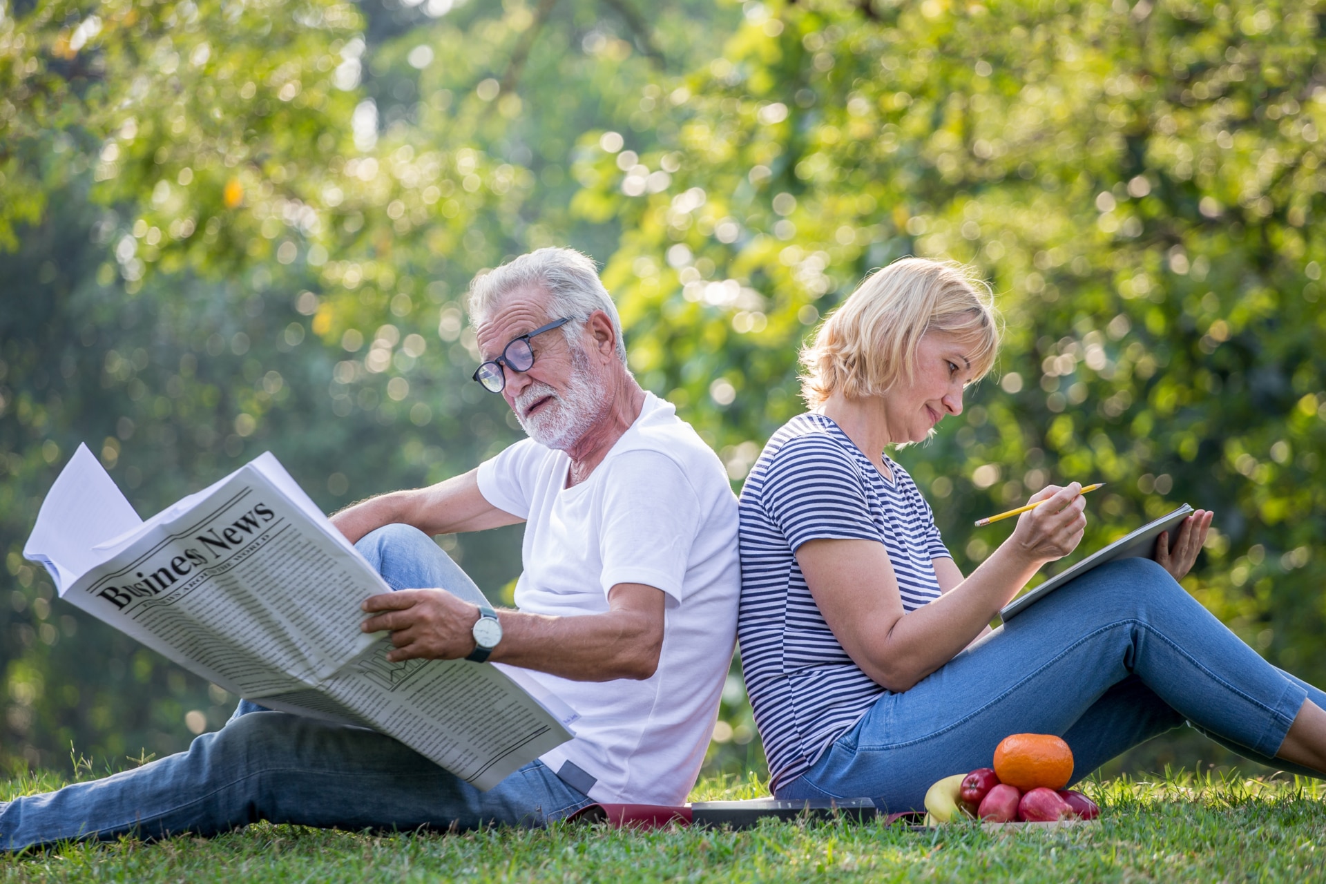 Happy senior couple relaxing sitting back to back in park reading newspaper and take write notes to Diary book  to together . old people in the summer park . Elderly resting .mature relationships .