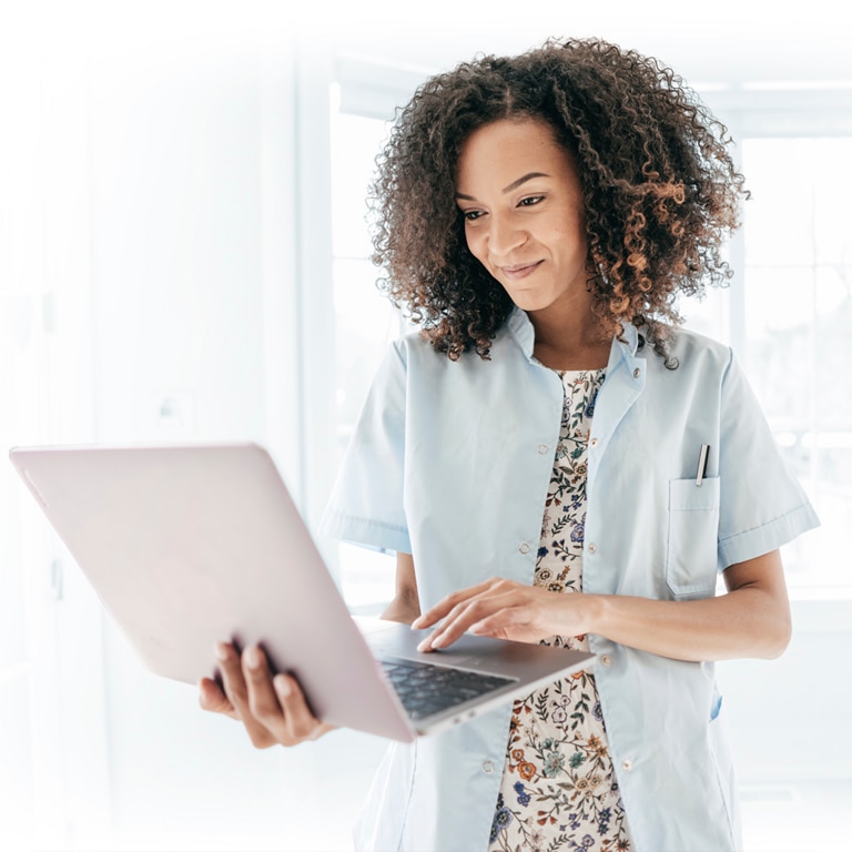Woman standing indoors with her laptop in hand. ph-pic-phonak-ab-cobranding-social-media-in-audiologist-01