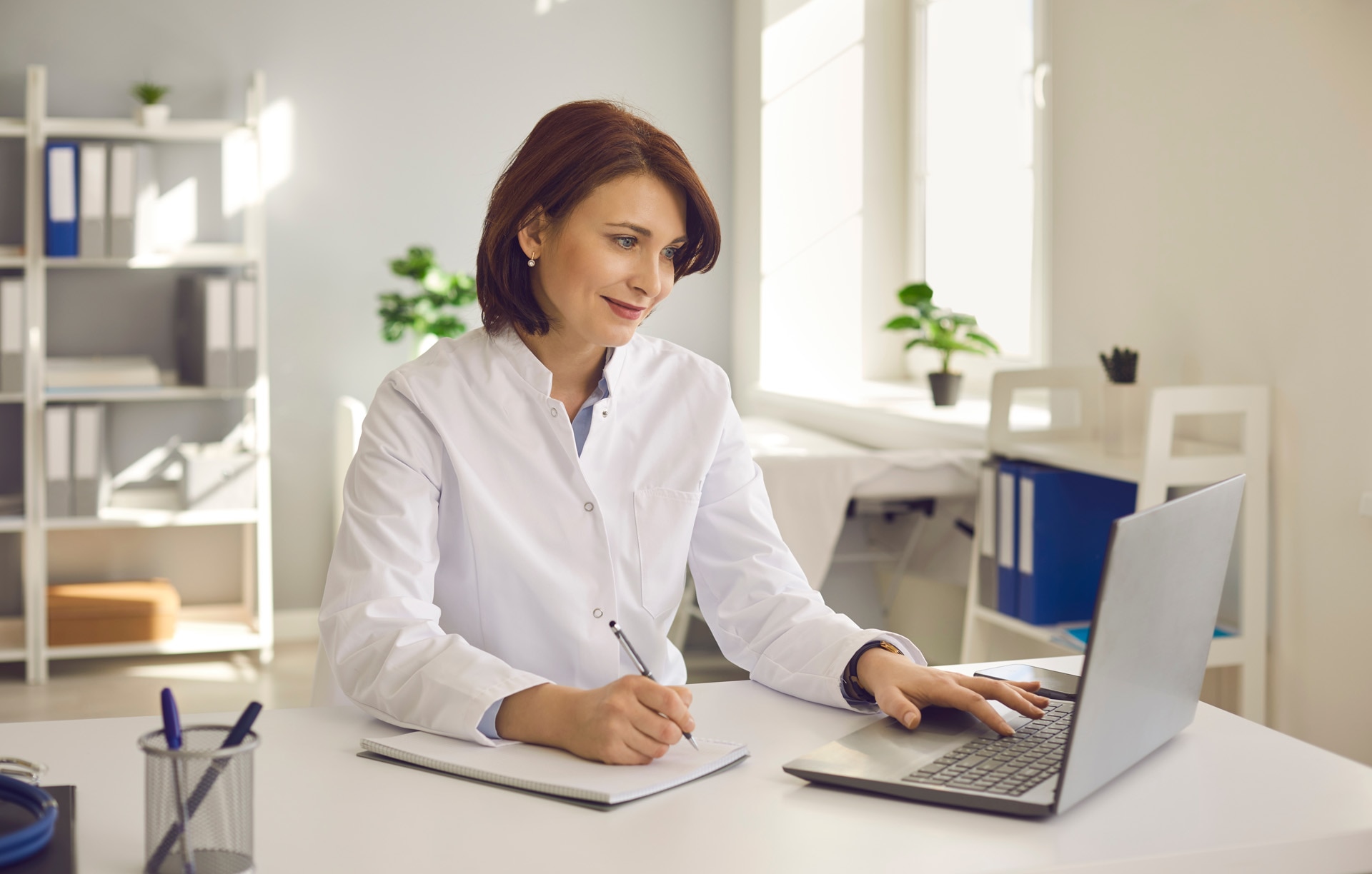 Une médecin prend des notes alors qu’elle suit un webinaire en ligne ou un séminaire de formation tout en étant assise avec un ordinateur portable sur son lieu de travail. Un médecin fait de son mieux pour proposer des soins médicaux de qualité