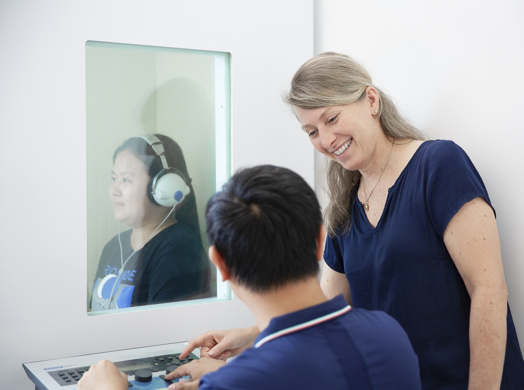 Audiologists testing sound on woman with headphones on through a window