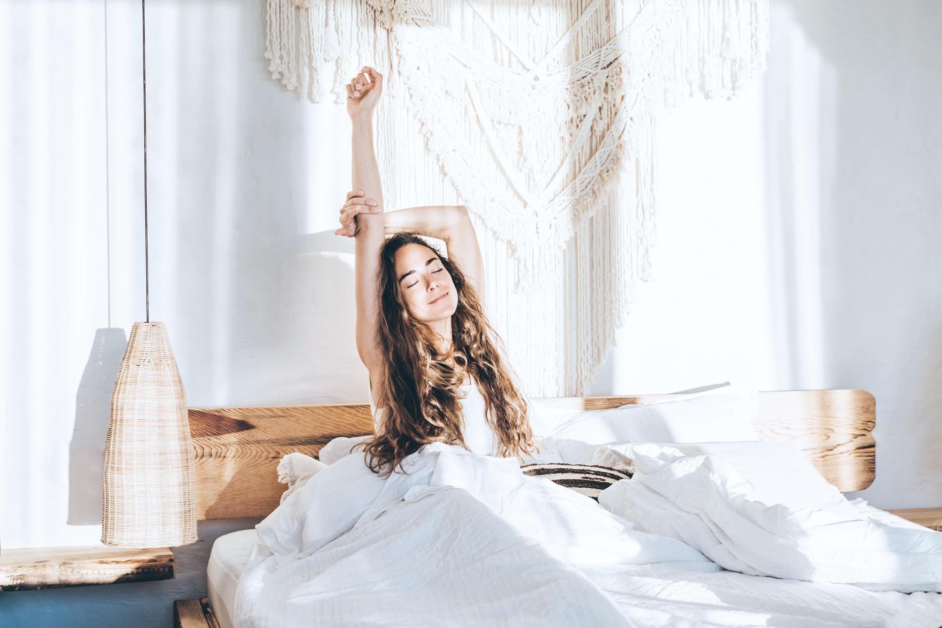 1387328216 Vrouw ontspant op bed. Vrouw die handen in bed uitrekt