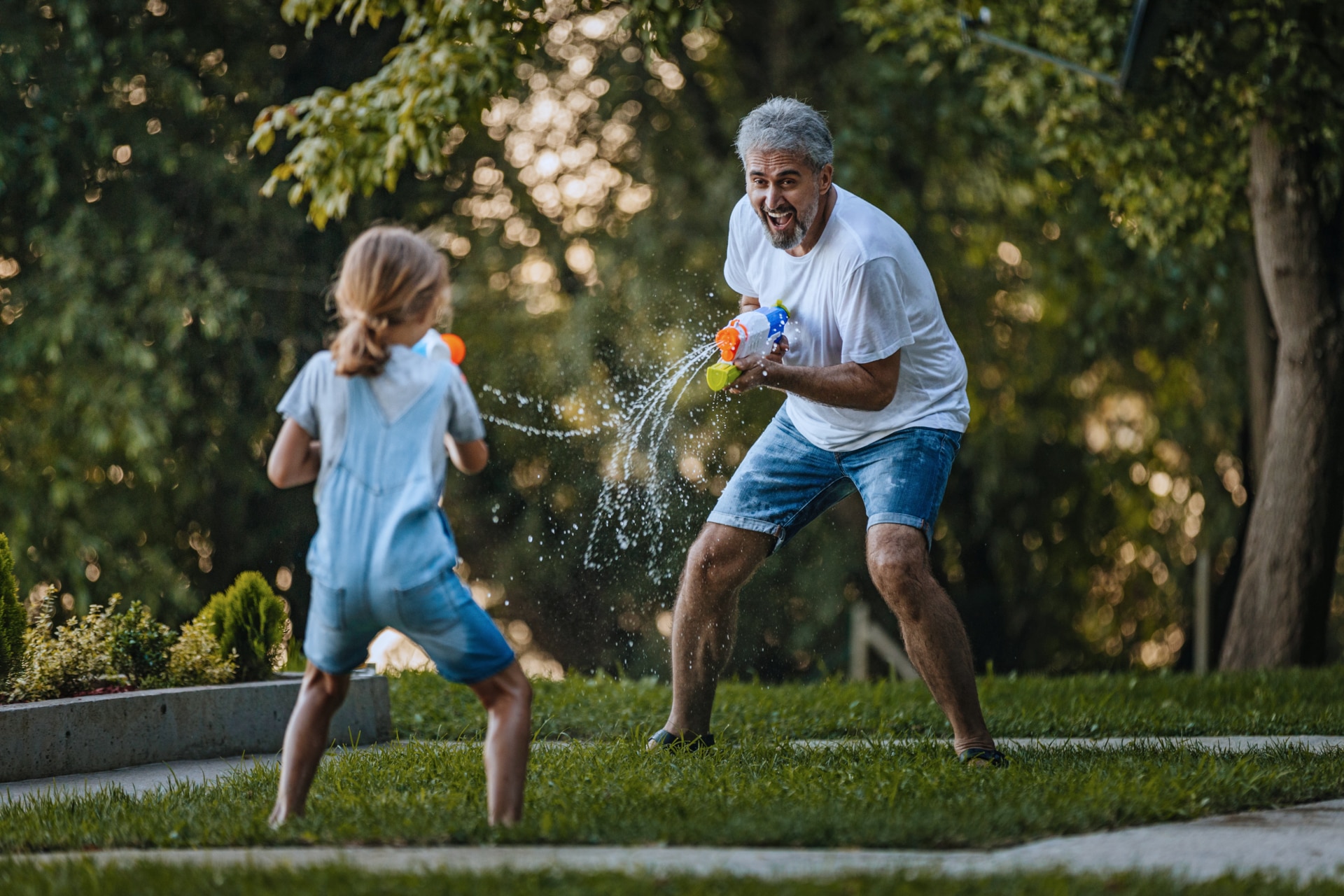 Vänskaplig vattenpistolstrid i en trädgård mellan en farfar och hans barnbarn.