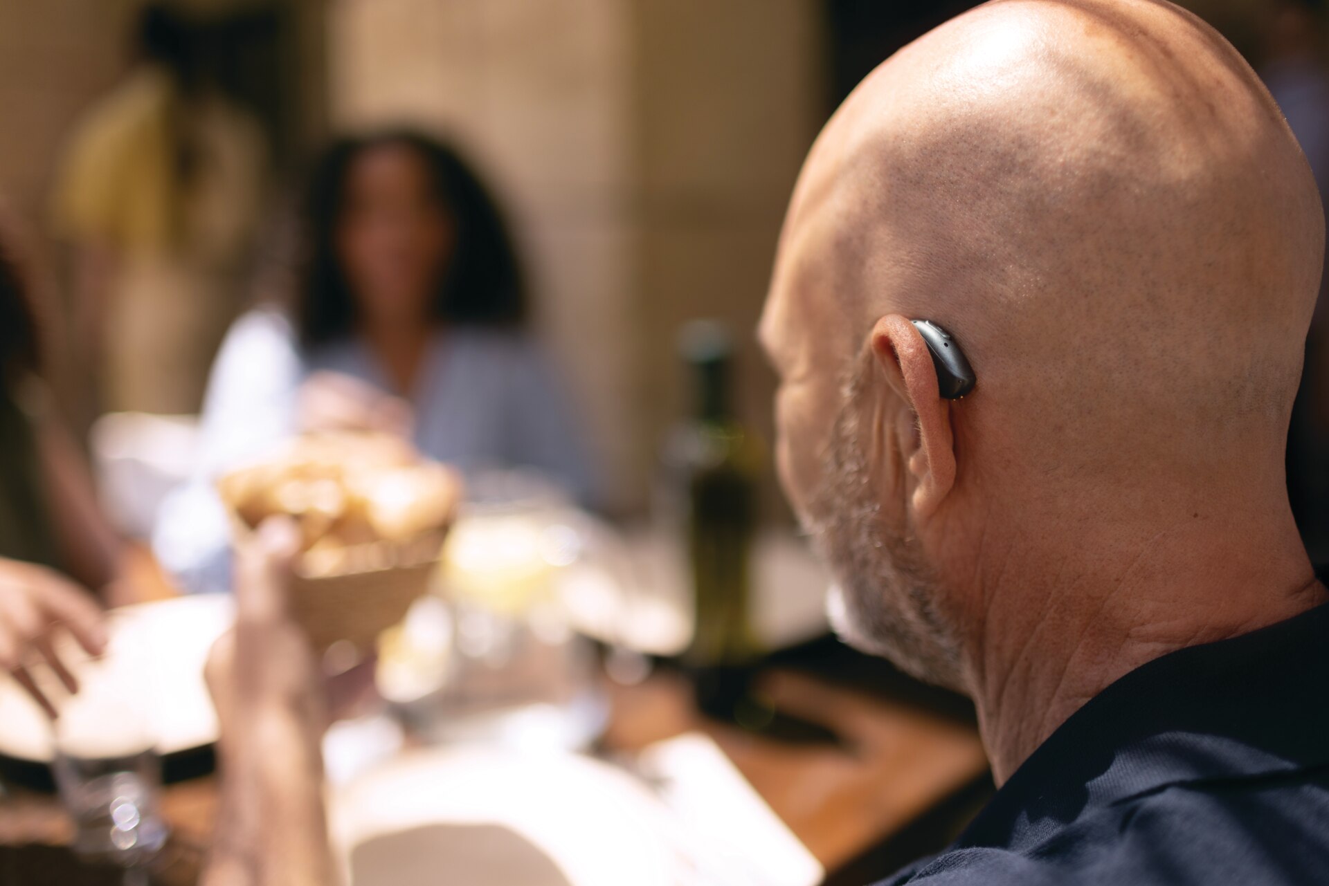 Man at restaurant table wearing Phonak Sphere Infinio hearing aids Close up of Sphere Infinio hearing aid behind the ear on a man
