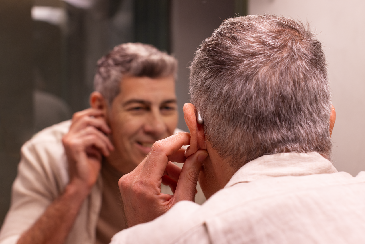 Man in the mirror adjusting his hearing aid